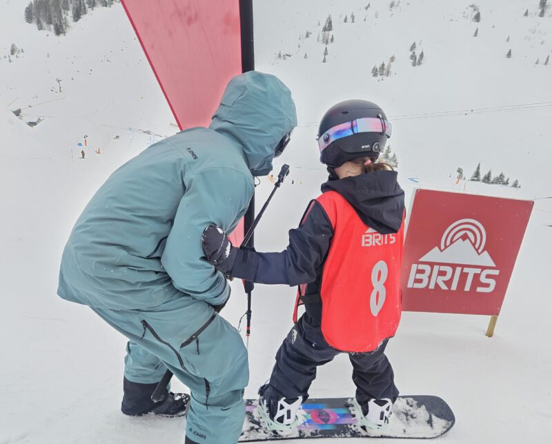Coach Euan Baxter at the 2026 Futures Championship big air start line with 8-year-old Coralie Thompson. Image © PlanetSKI